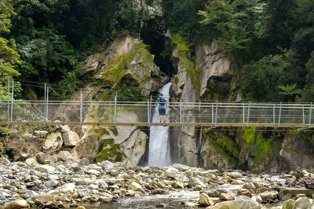 Hiker standing on a bridge in front of Giant Gate Fall on the Milford Track