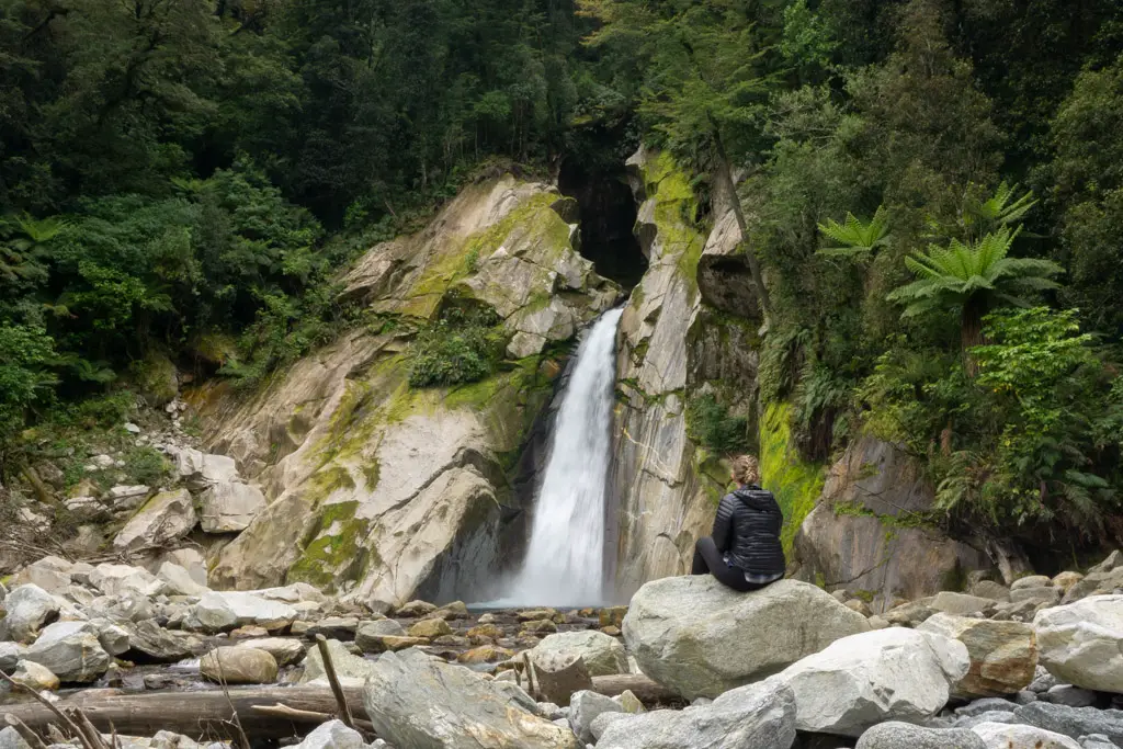 Woman sitting on a rock in front of Giant Gate Falls on a day walk along the Milford Track with Fiordland Outdoors in Fiordland National Park
