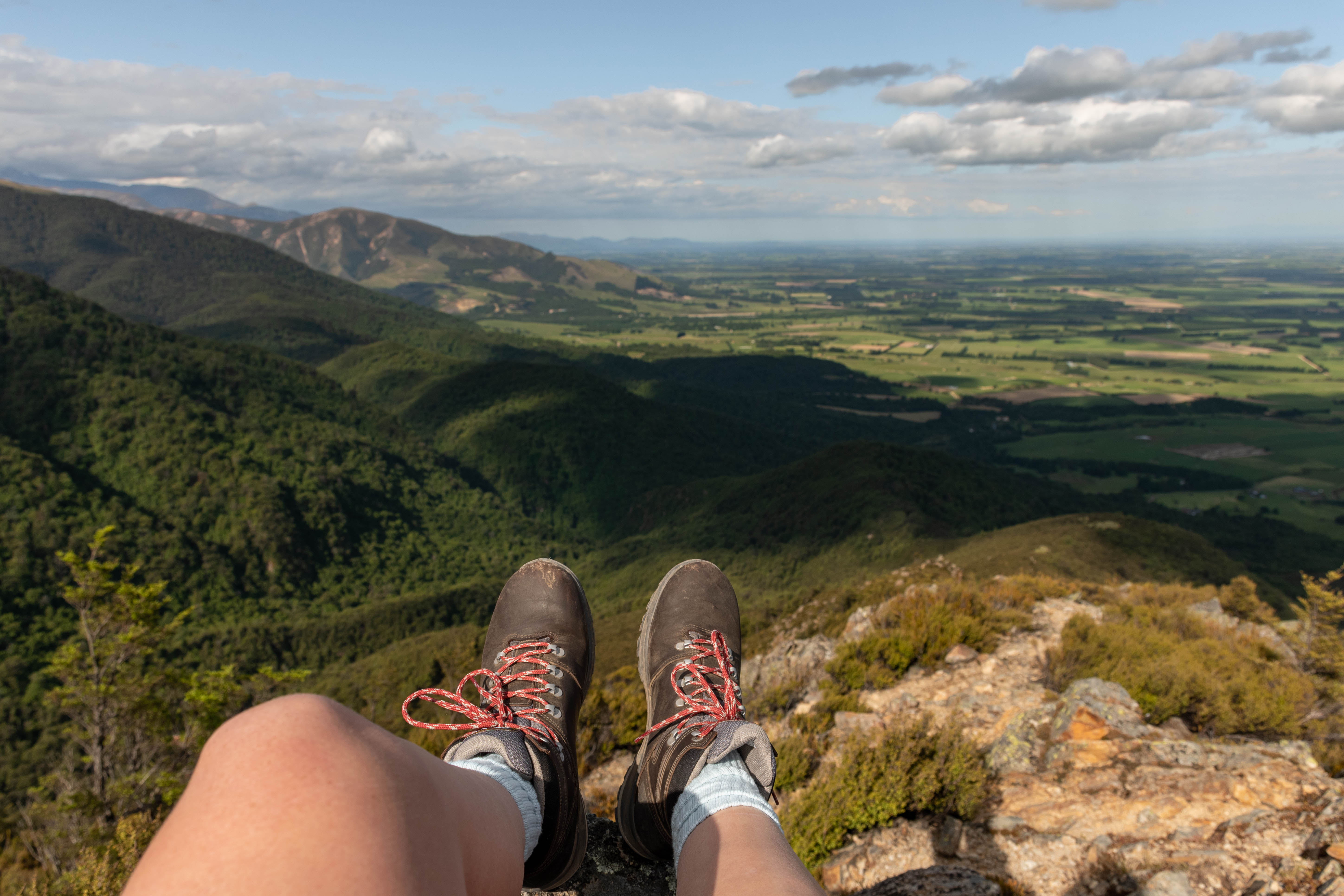Photo of tramping boots and legs sitting on a tussock mountain top