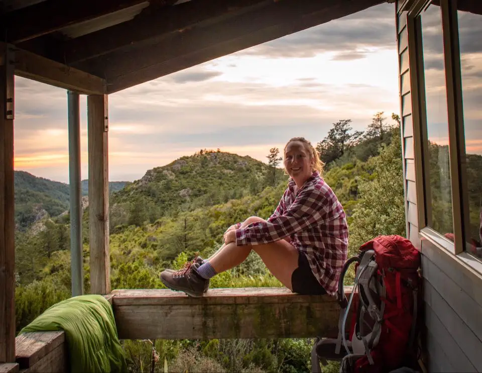 Adult sitting on the balcony of a tramping hut at sunset