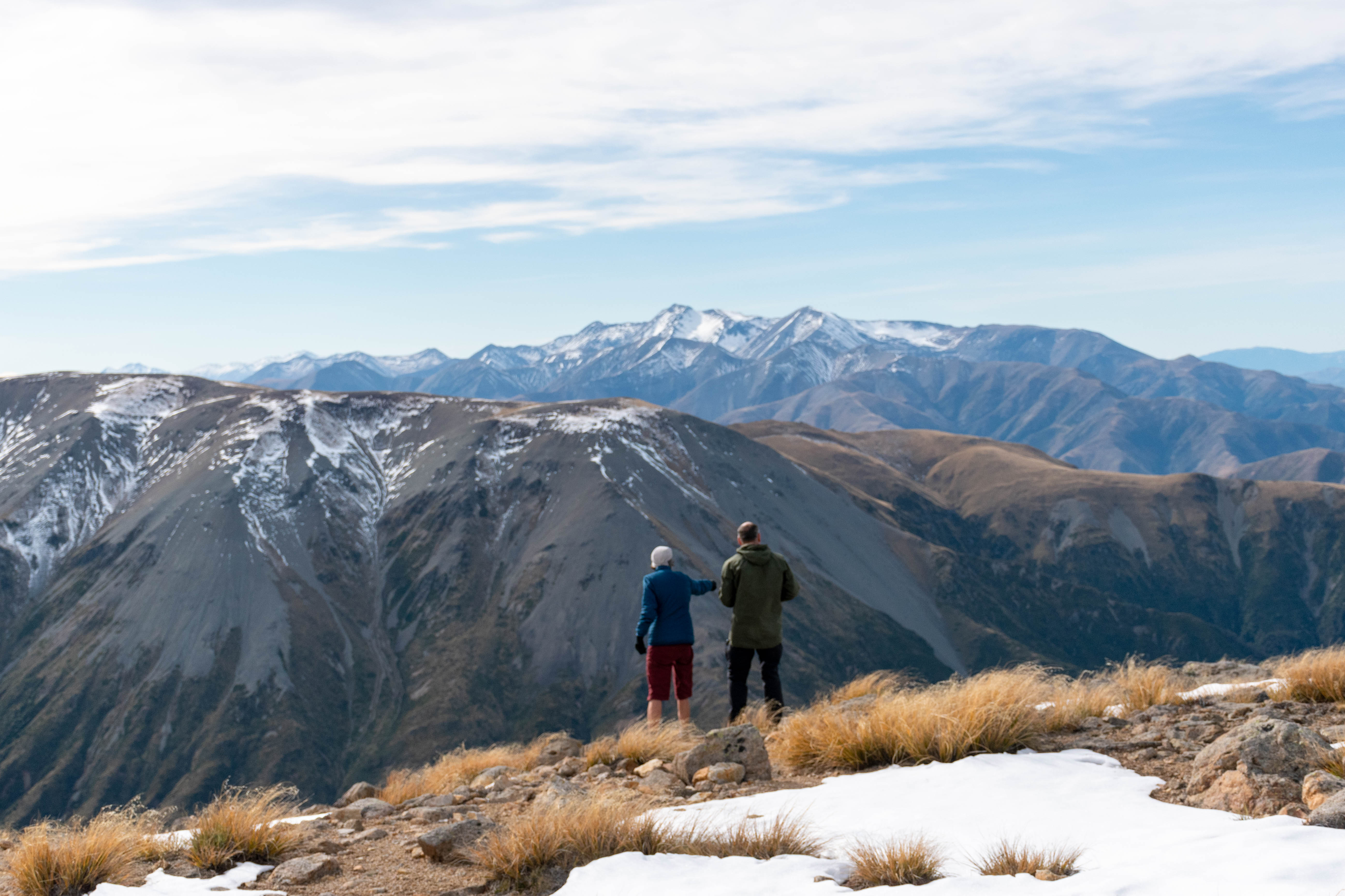 Two adults standing in front of snowy mountains on a tramping track