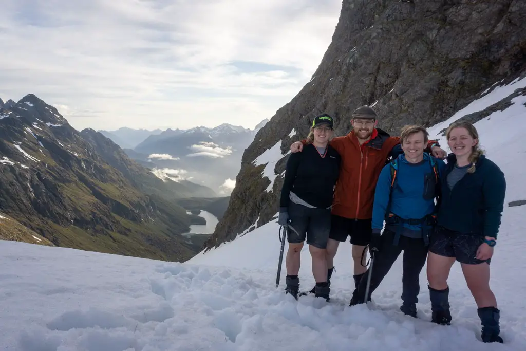 Four trampers posing for photo in snow at the to top of Emily Pass, with Lake Mackenzie in the background