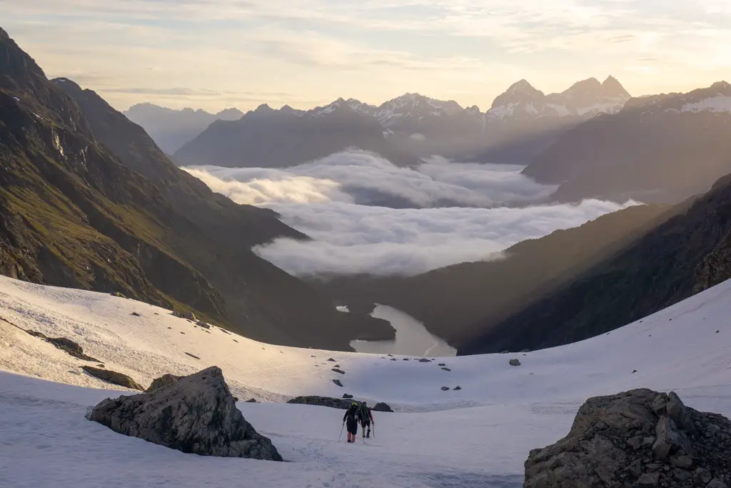 Trampers climbing down snow slopes from Emily Pass with an inversion layer over Lake Mackenzie on the Routeburn Track