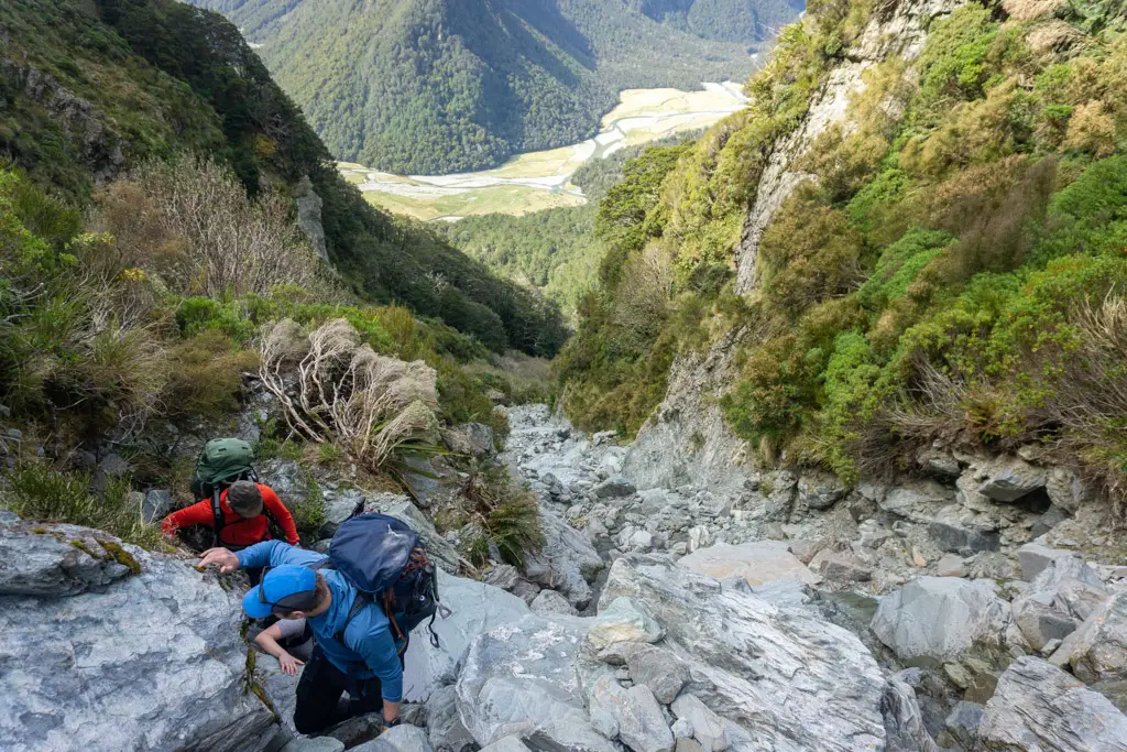 Three trampers climbing up a steep section of Emily Creek towards Emily Pass with Routeburn Flats in the background below