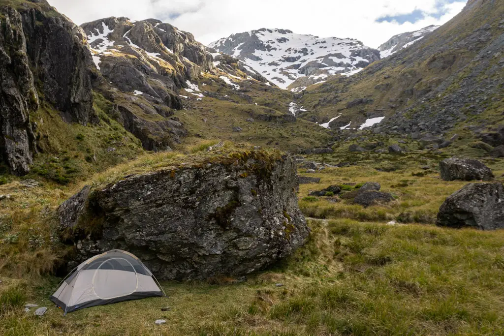 Tent next to a boulder with snowy mountains behind it