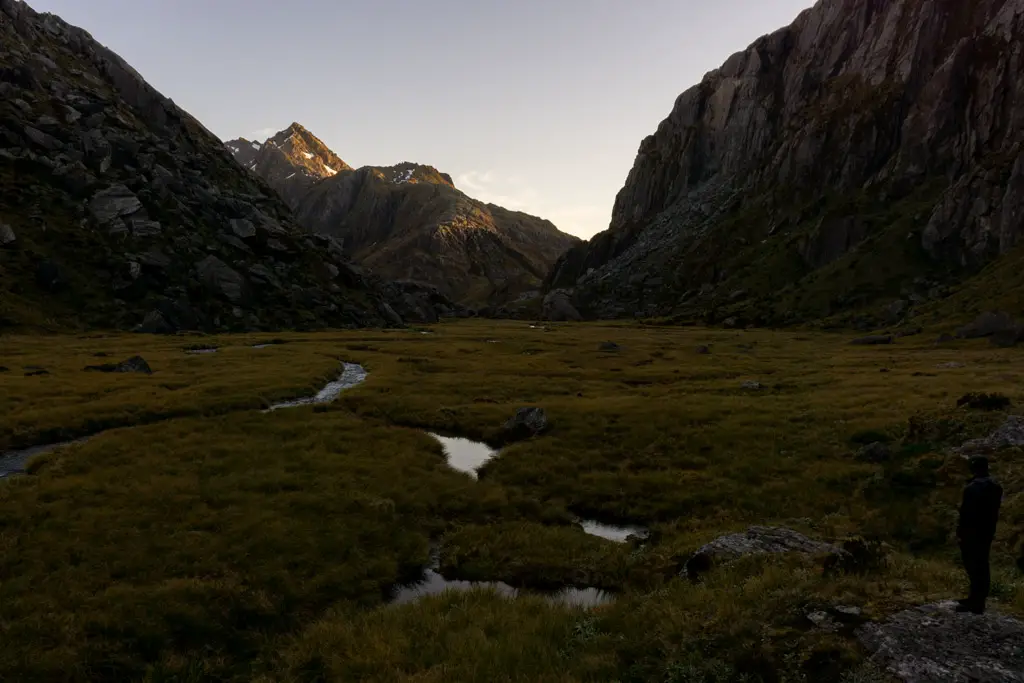 Tramper standing on a rock at sunset, looking out at Valley of the Trolls towards Ocean Peak and the Routeburn Track