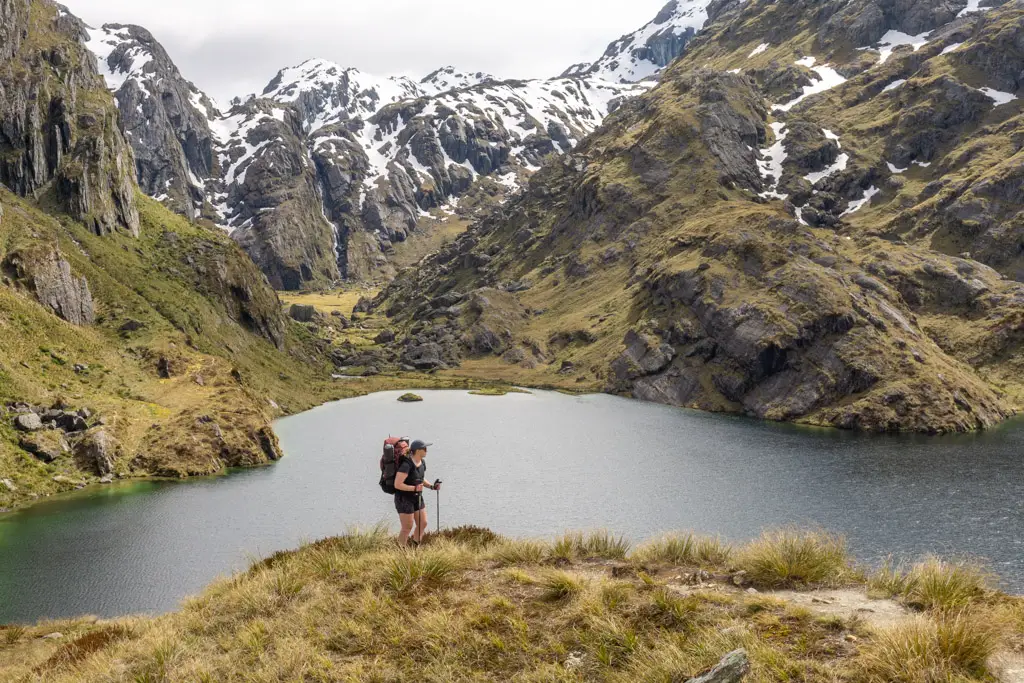 Female tramper walking along the Routeburn Track with poles, with Valley of the Trolls in the background