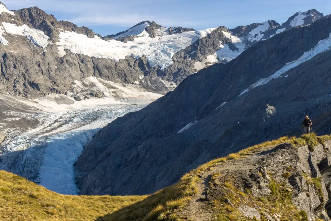 Man walking along the Cascade Saddle Route with the Dart Glacier in the background
