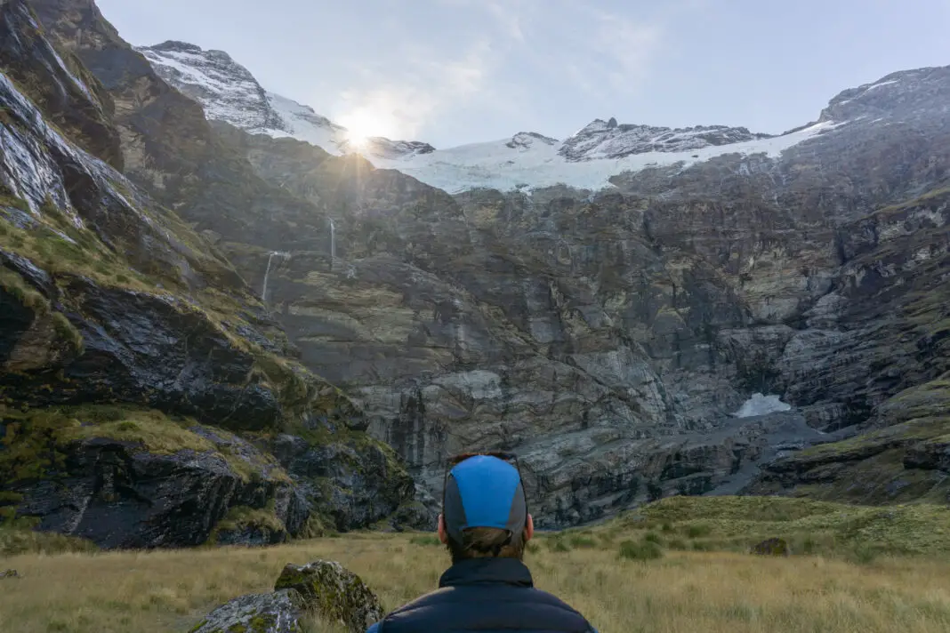 Back of a man's head wearing a blue cap, staring up at the Earnslaw Burn cirque with frozen waterfalls and hanging glaciers