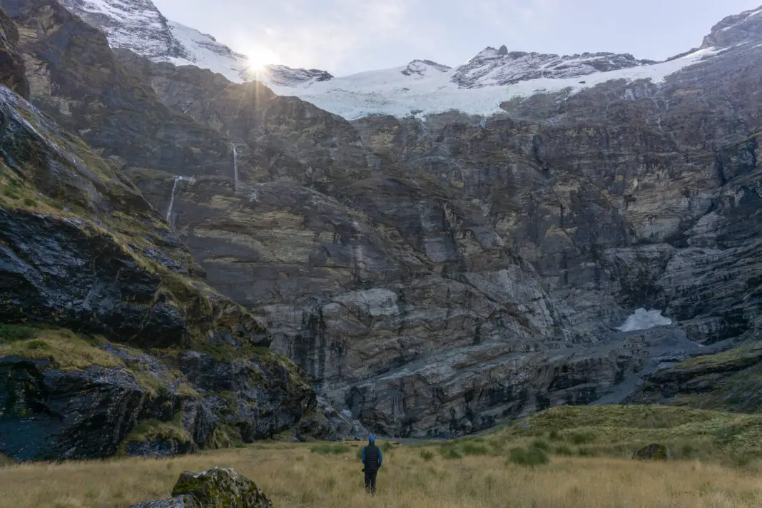 Man standing beneath the hanging glaciers and waterfalls at the head of the Earnslaw Burn valley