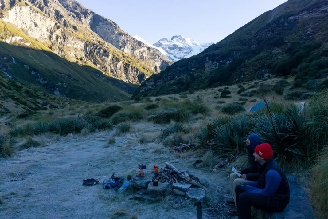 Trampers sit in a frozen campsite with Mt Earnslaw in the background