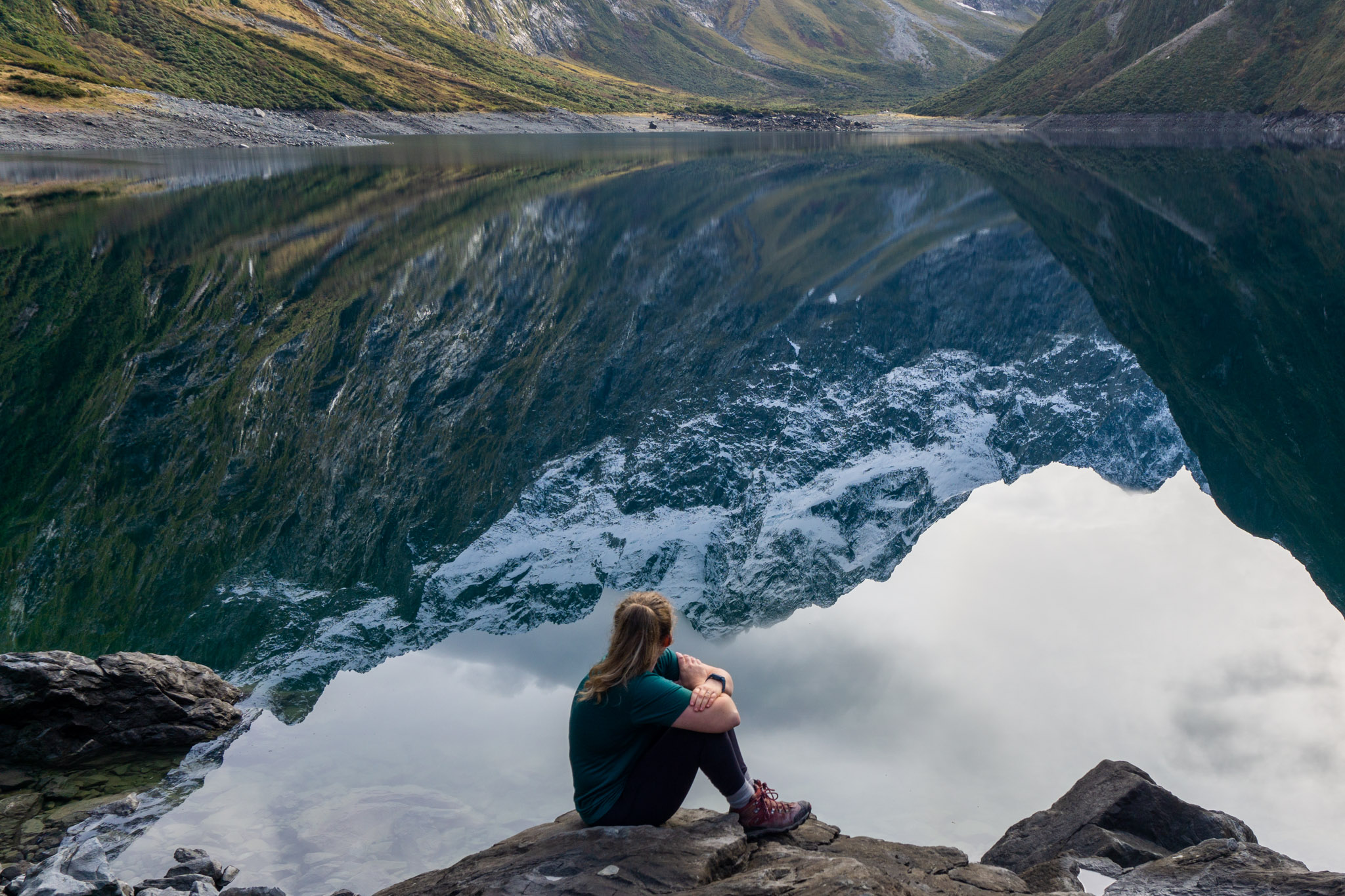 Woman sitting in front of a reflective alpine lake wearing an Ottie Merino t-shirt