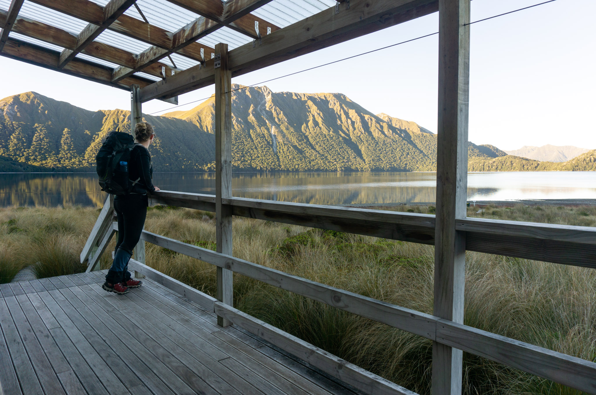 Tramper standing on the deck of Green Lake Hut watching the sunrise
