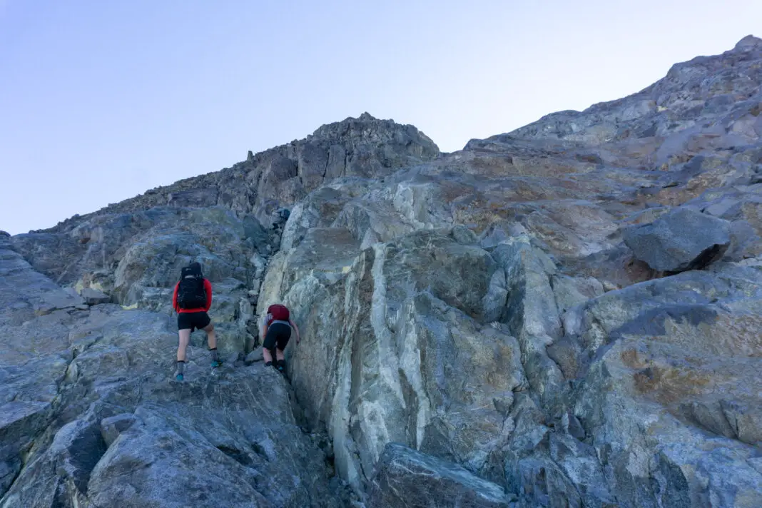 Three trampers climbing up rock slabs to Barrier Knob