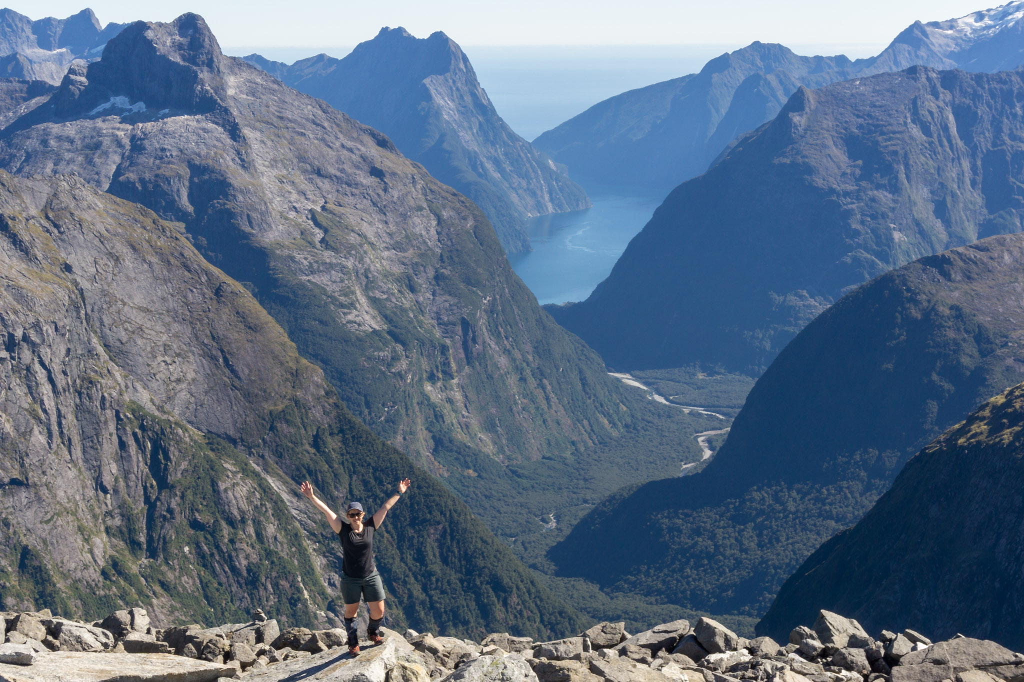 Woman standing on top of Barrier Knob in Fiordland National Park with Milford Sound in the background
