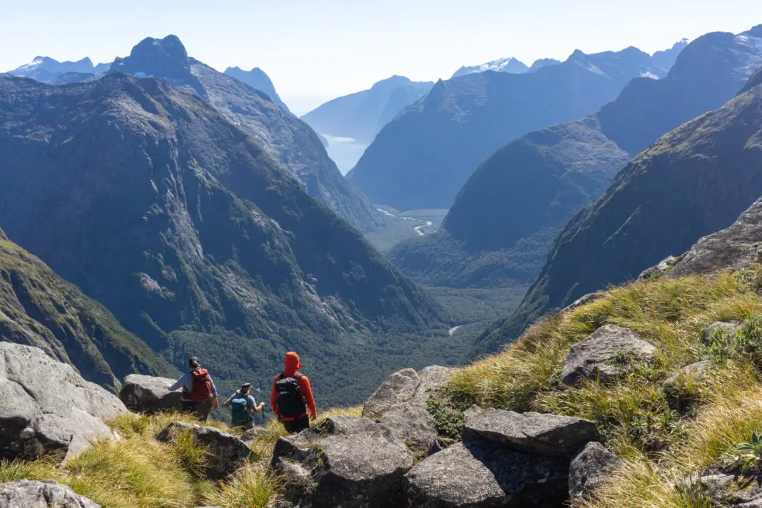 Three trampers climbing down to Gertrude Saddle with Milford Sound in the background