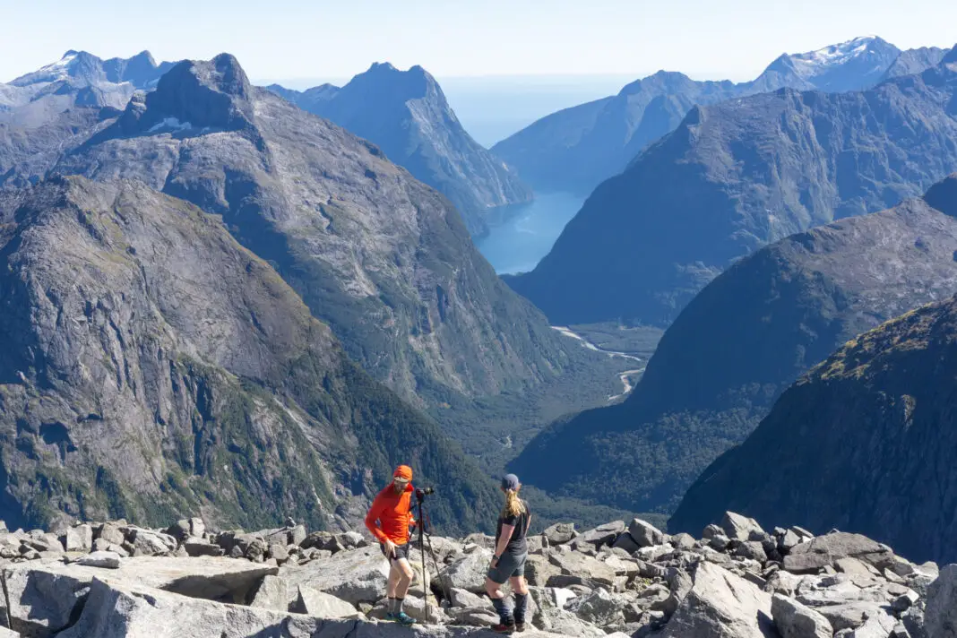 Two trampers standing on the summit of Barrier Knob with Milford Sound in the background