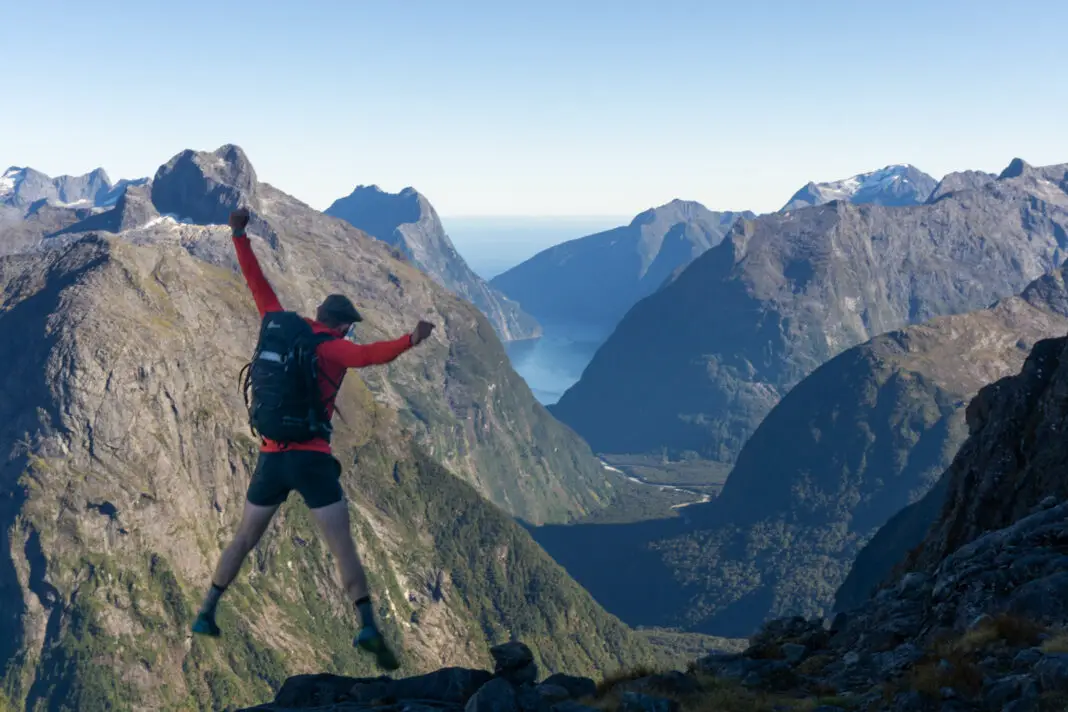 Man jumping on top of Gertrude Saddle with views of Milford Sound in the background