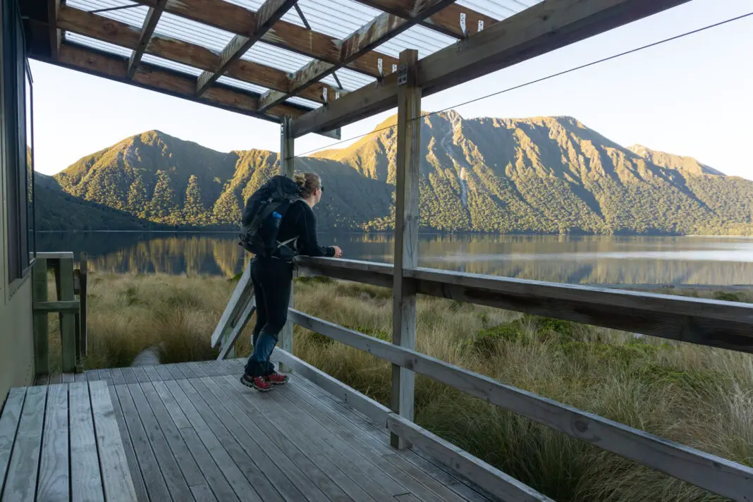 Woman standing on the deck of Green Lake Hut with the lake and mountains in the background