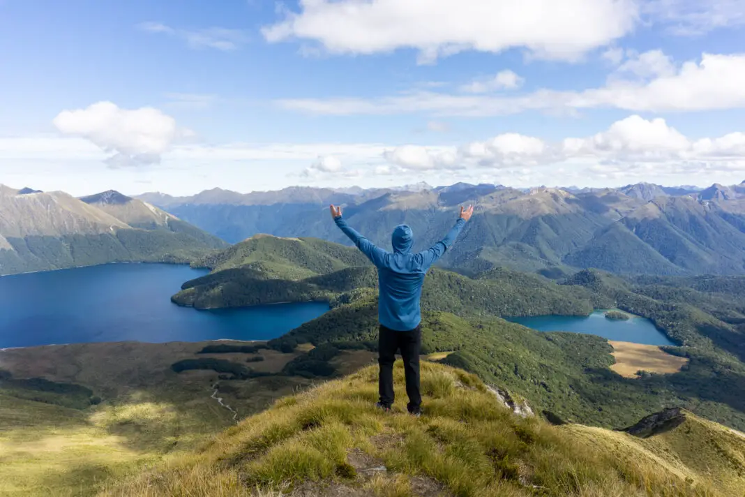 Man with arms up in the air with Green Lake and Island Lake below him in the background