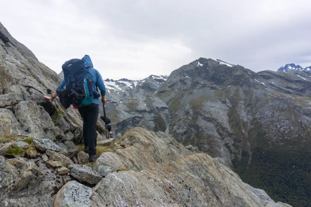 Man climbing around a rocky ridge above Lake Nerine towards Park Pass