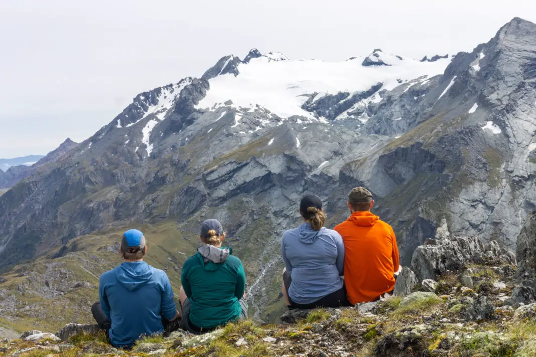 Four trampers sitting near Lake Nerine looking towards Park Pass and Park Pass Glacier