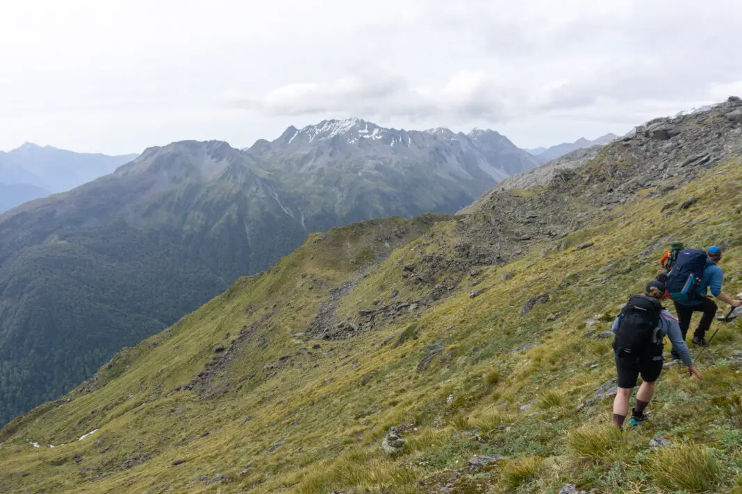 Three trampers traversing tussock from North Col to Lake Nerine