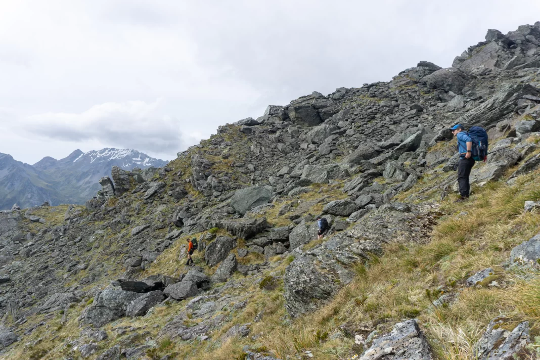 Three trampers traversing tussock and rocks from North Col to Lake Nerine