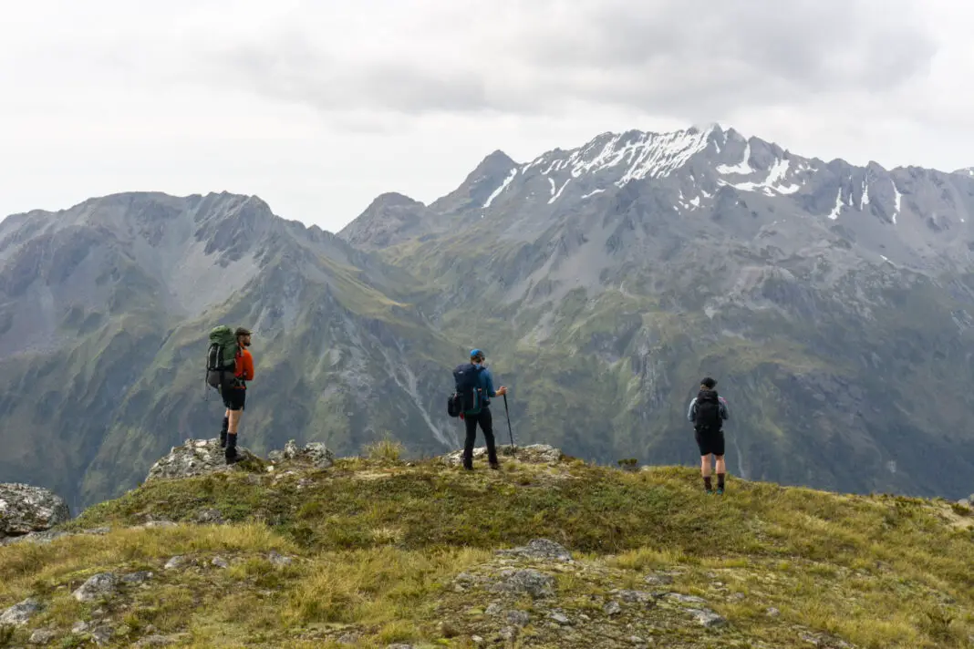 Three trampers standing on a tussock terrace near North Col and Lake Nerine