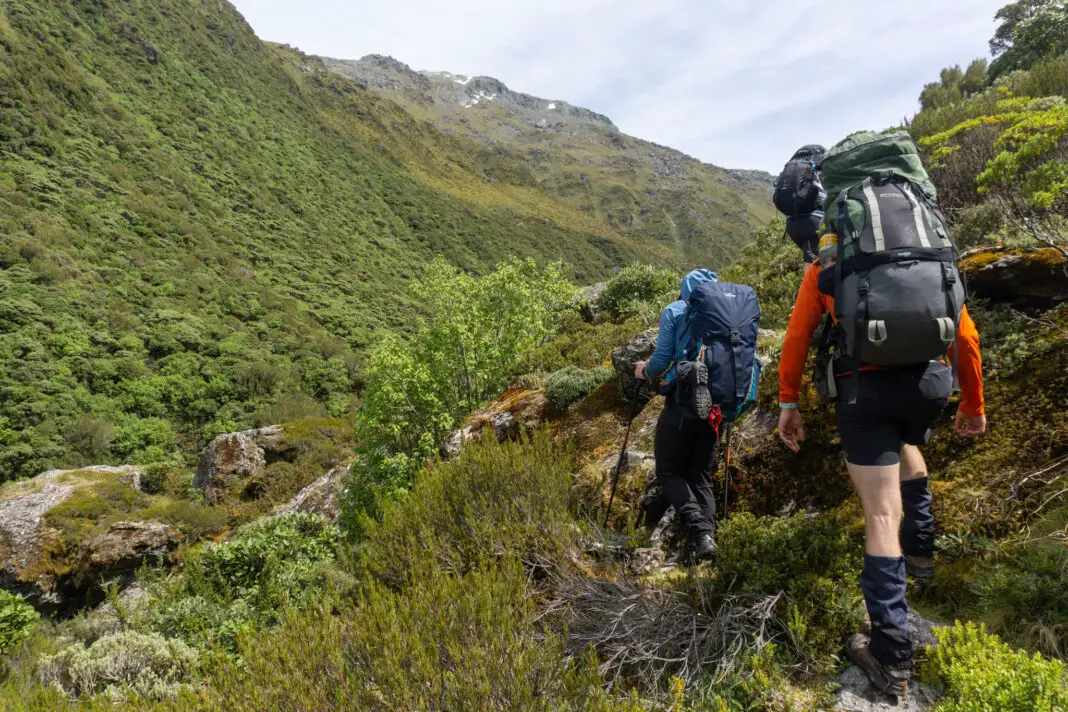 Trampers climbing through boulders and scrub