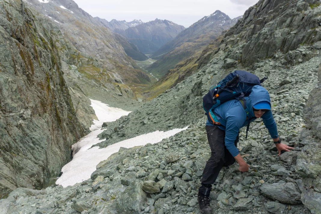 Man climbing up a scree and snow slope to North Col with Routeburn Flats in the background