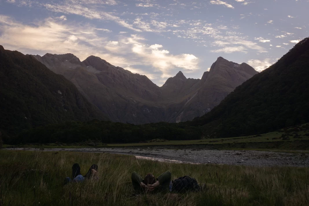 Two people lying down in grass as the sun sets on the mountains above Routeburn Flats Hut
