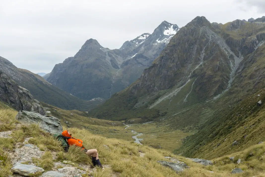 Tramper lying in tussocks on Park Pass looking toward Theatre Flat