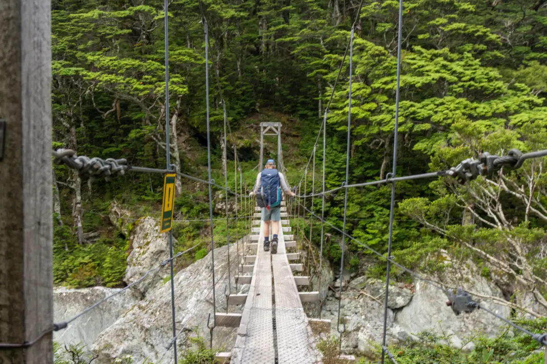 Tramper walking across a swing bridge across the Rockburn near Theatre Flat