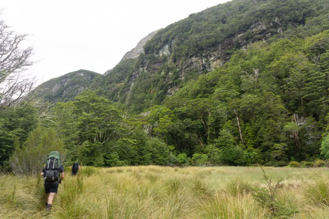 Trampers walking from Theatre Flat along the Rockburn Valley with cliffs above them