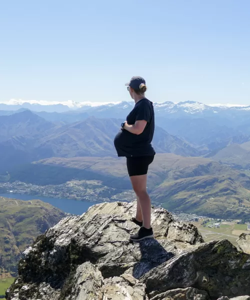 Pregnant woman standing on top of a mountain looking at the view