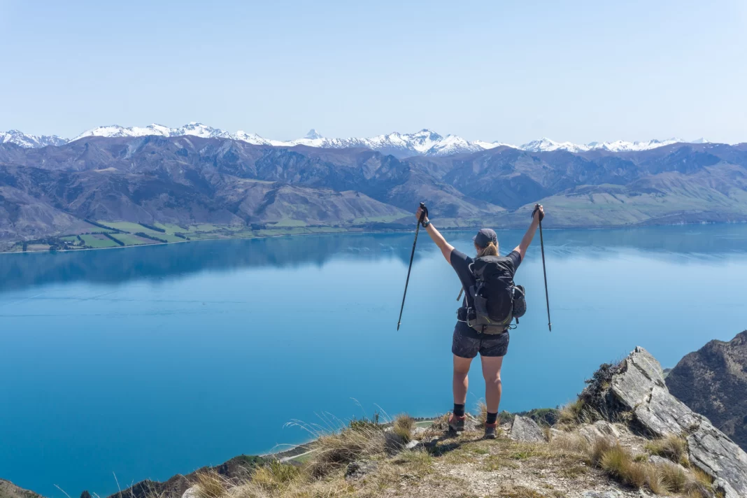 Pregnant woman holding poles up in the air on top of mountain with lake and mountains in the background