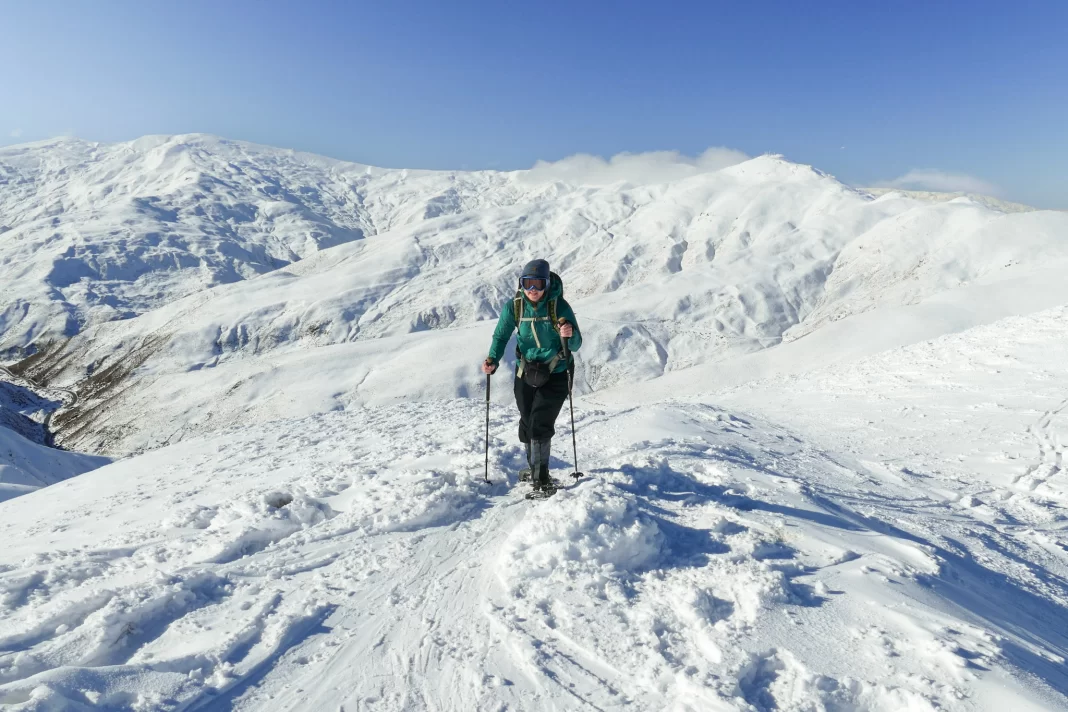 Pregnant woman snowshoeing up a mountain with snowy mountains in the background