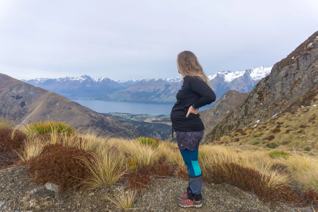 Pregnant woman standing on a tramping track looking out at the view of Lake Whakitipu