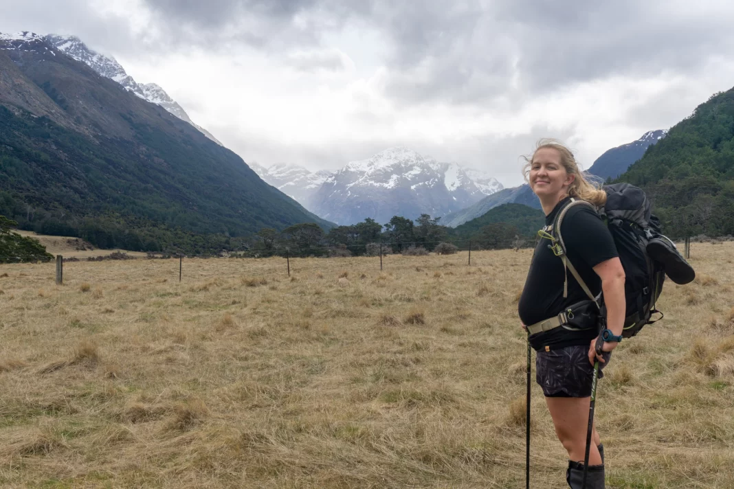 Pregnant woman smiling at camera wearing a tramping pack with mountains in the background