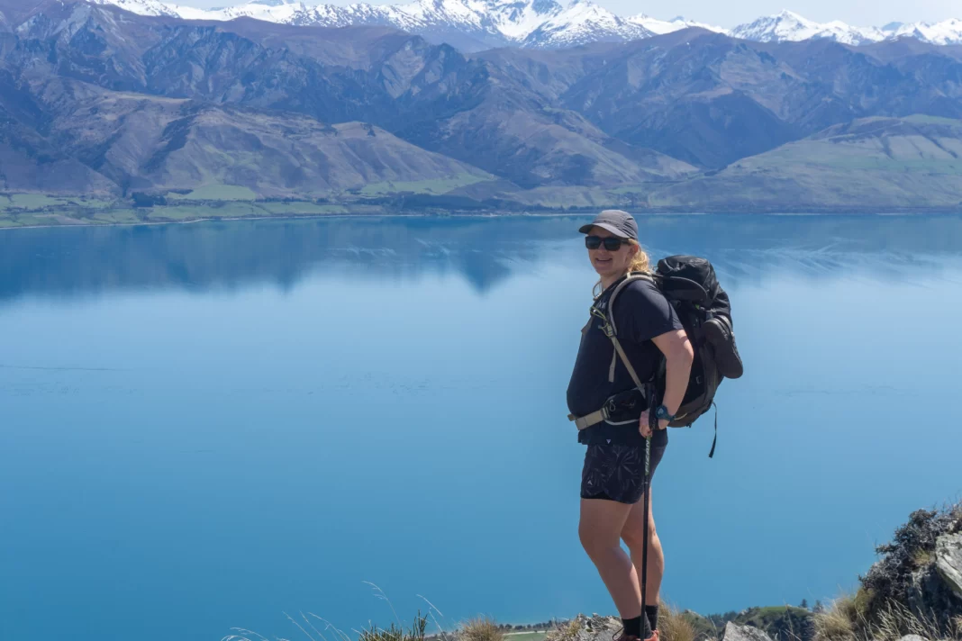 Pregnant woman wearing a backpack with lake and mountains behind her