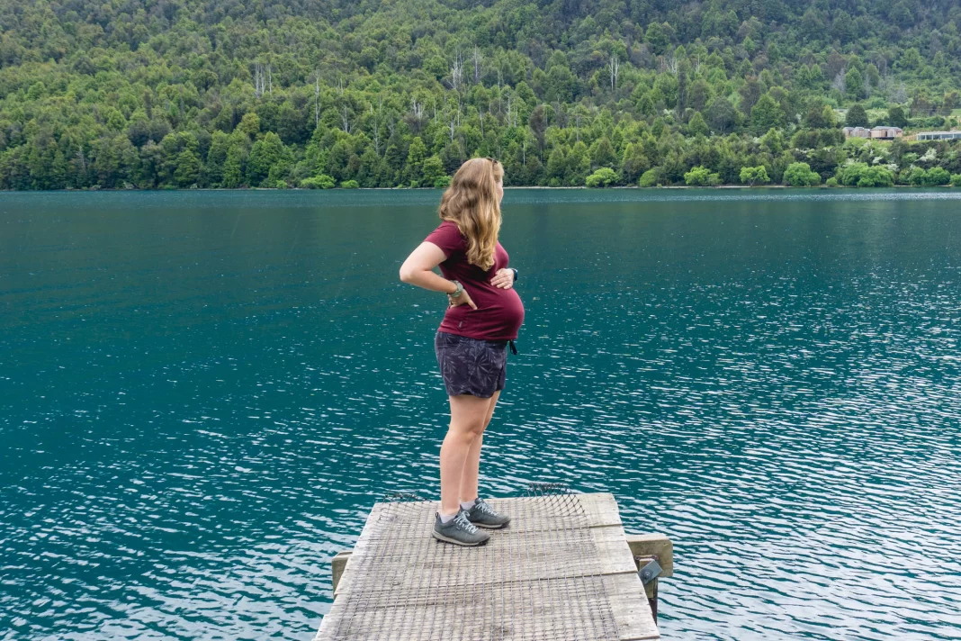 Pregnant woman standing on small wharf at Bob's Cove with aqua lake and trees in the background