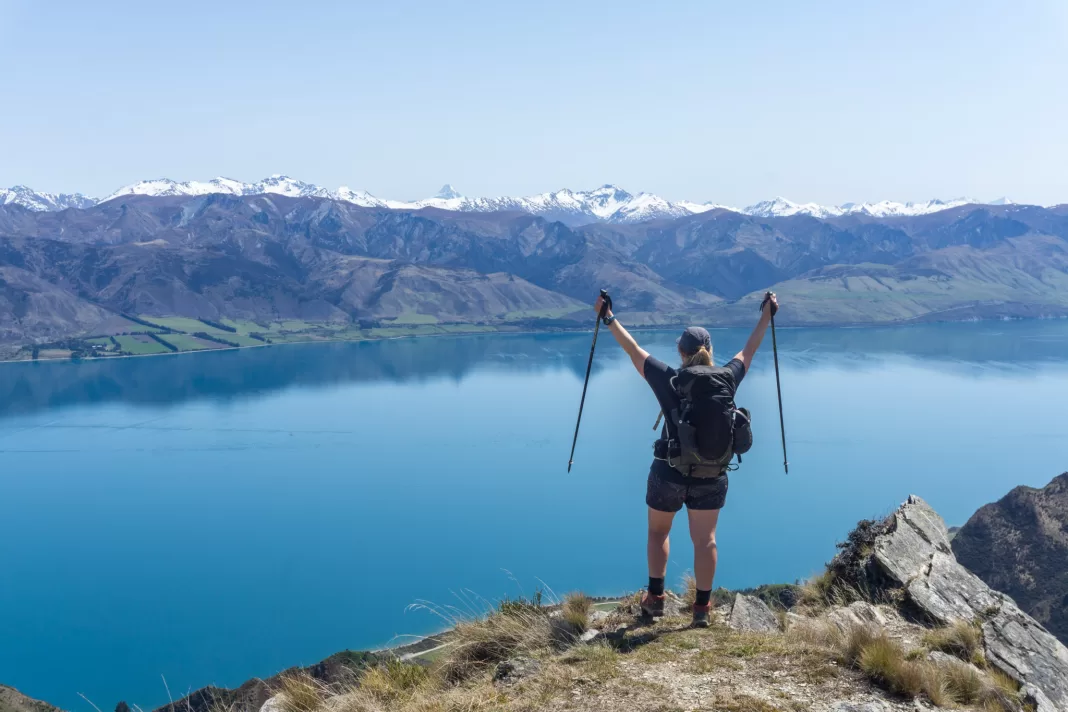 Woman standing with arms and poles raised with Lake Hawea and mountains in the background