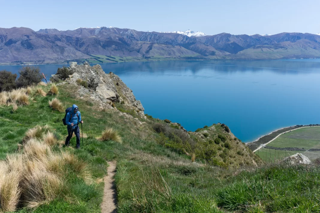 Man walking along the Breast Hill Track with Lake Hawea in the background