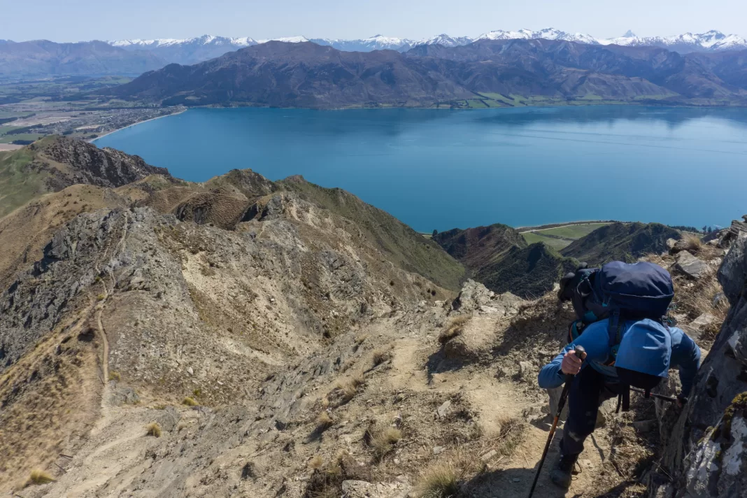 Man climbing up Breast Hill Track with Lake Hawea and mountains in background