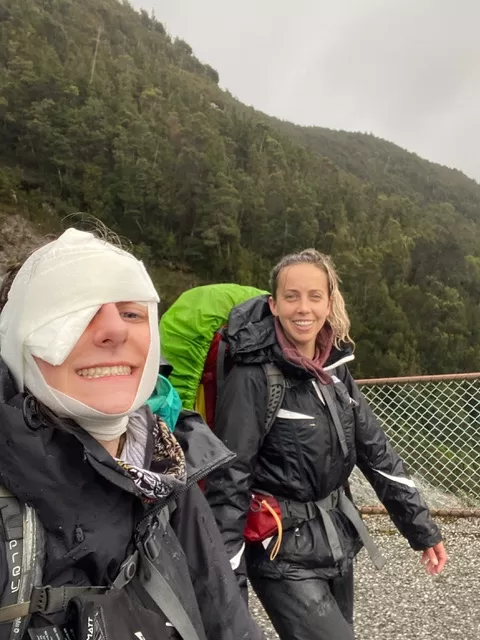 Two women hiking, one with a bandage over her injured eyelid while attempting a self-rescue