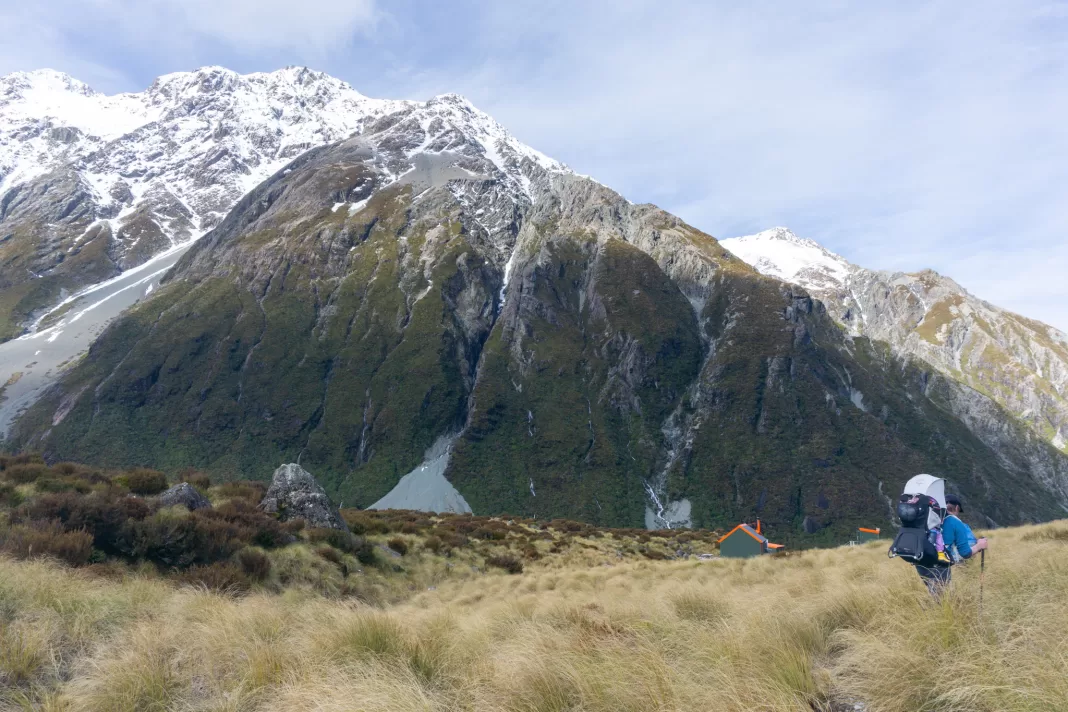 Photo of hiker walking towards Hooker Hut with mountains in the distance