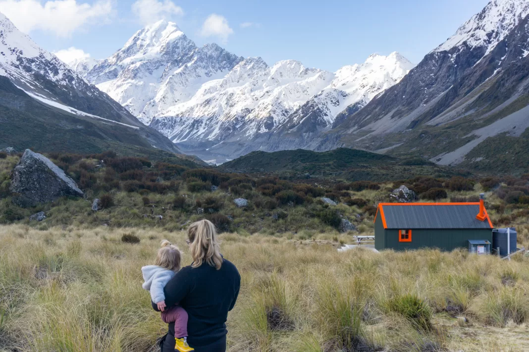 Photo of a woman holding her toddler near Hooker Hut, looking at Aoraki Mt Cook in the distance