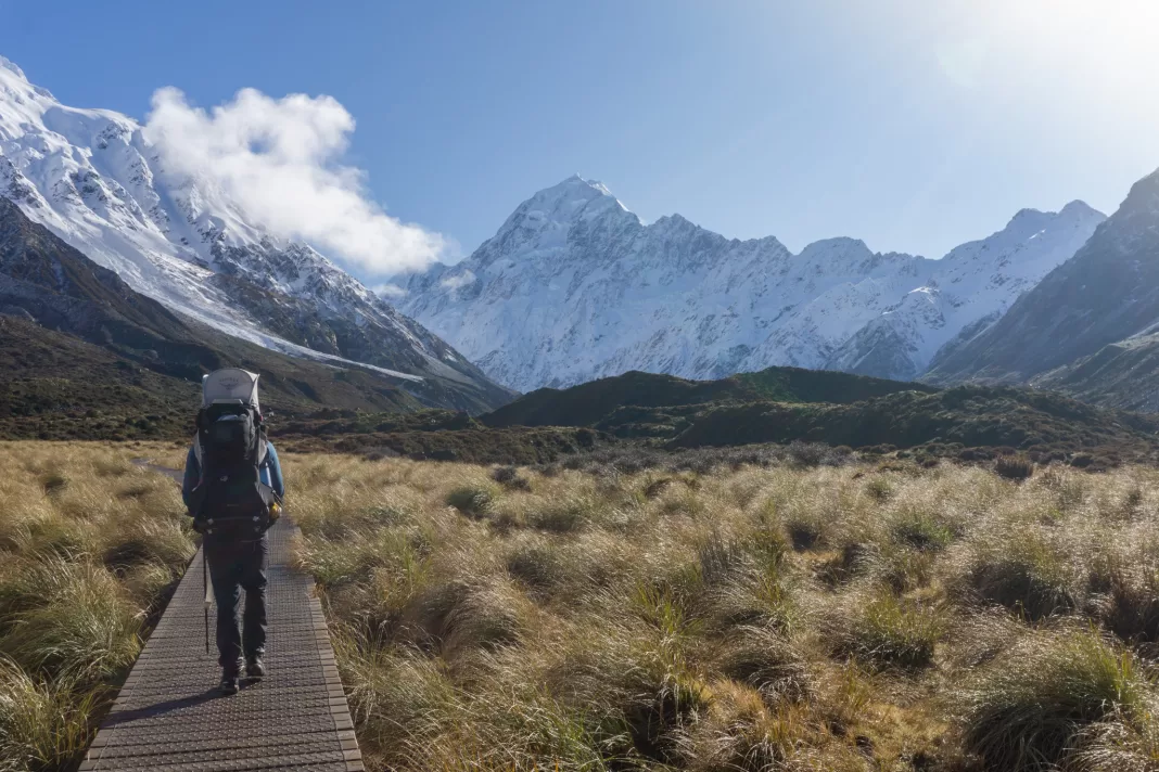 Man with a baby backpack walking on boardwalk on the Hooker Valley Track with Aoraki Mt Cook in the background