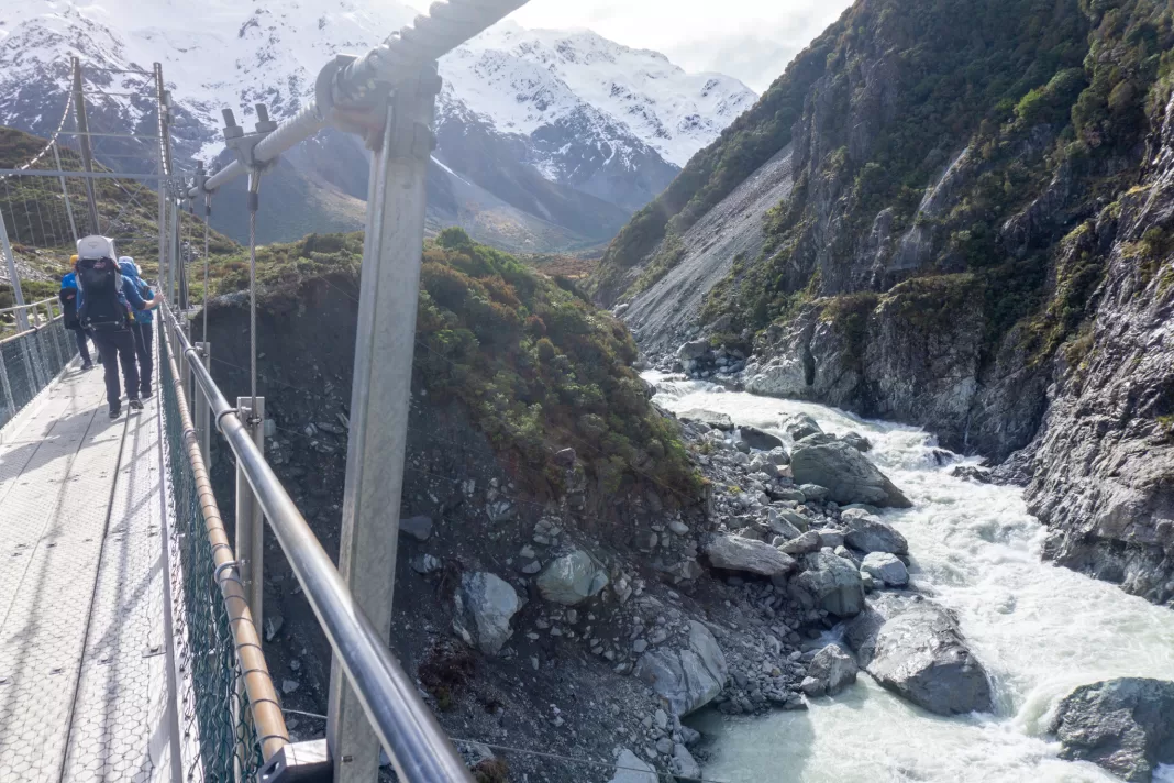 Hikers walking over a swing bridge on the Hooker Valley Track